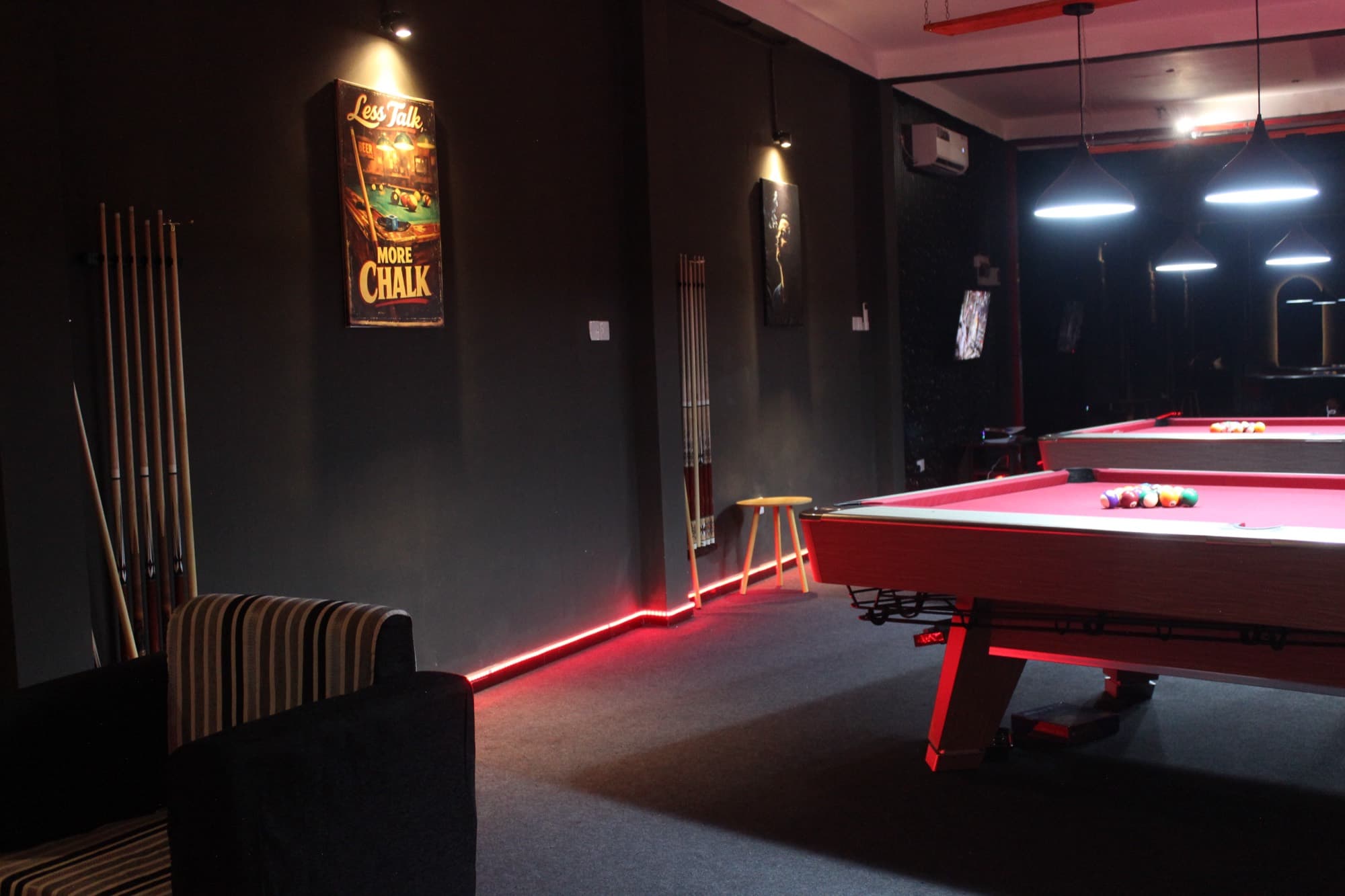 Two pool tables with seating between them under warm lamps